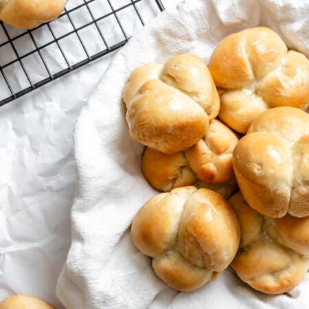 A flour sack lined basket of rolls next to a couple of rolls.