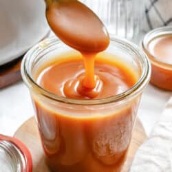 Caramel sauce drizzling from a spoon back into a jar of caramel sauce.