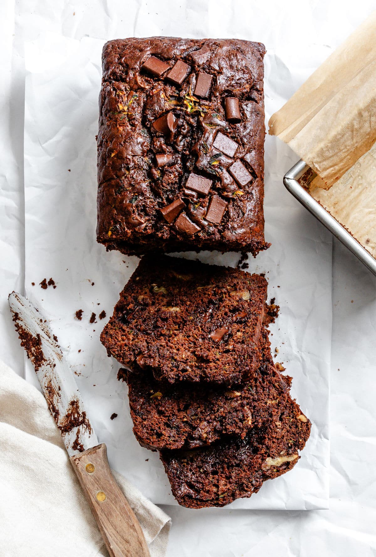 A loaf of chocolate zucchini bread with three slices next to it.