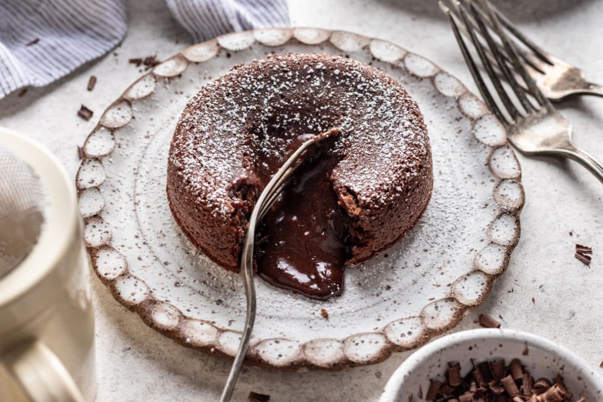 A molten chocolate cake on a plate with chocolate lava coming out of it.