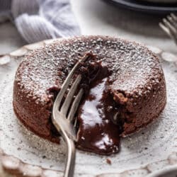 A silver fork cutting into a molten chocolate cake with chocolate running out.