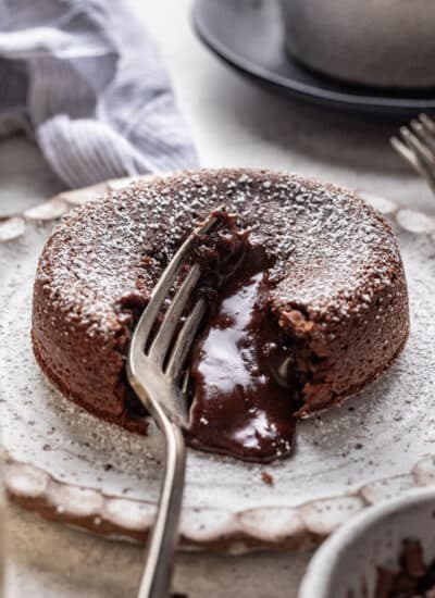 A silver fork cutting into a molten chocolate cake with chocolate running out.
