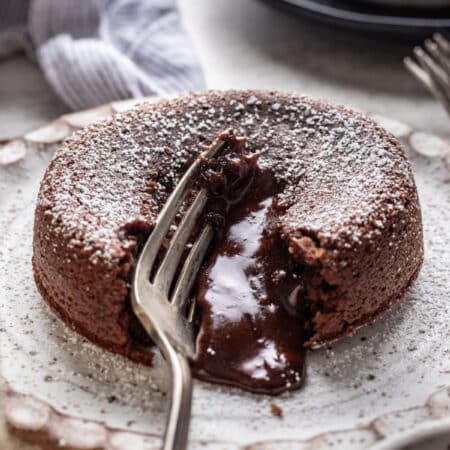 A silver fork cutting into a molten chocolate cake with chocolate running out.
