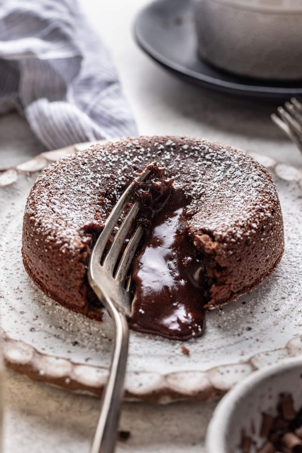 A silver fork cutting into a molten chocolate cake with chocolate running out.