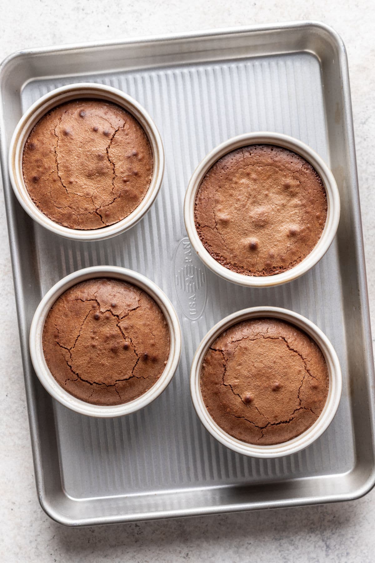 Baked molten chocolate cakes in ramekins on a baking tray.