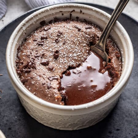 A molten chocolate cake in a ramekin with chocolate next to the spoon.