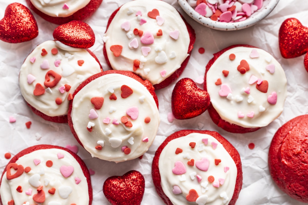 Red velvet cookies with cream cheese frosting next to red decorative hearts.