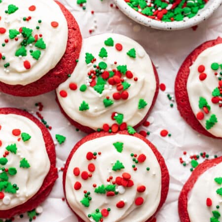 Red velvet cupcake cookies topped with Christmas sprinkles next to a dish of sprinkles.