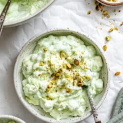 A bowl of Watergate salad topped with chopped pistachios next to a dish of chopped pistachios.