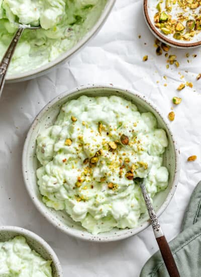 A bowl of Watergate salad topped with chopped pistachios next to a dish of chopped pistachios.