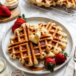 Two yeast waffles on a plate topped with pats of butter and strawberries.