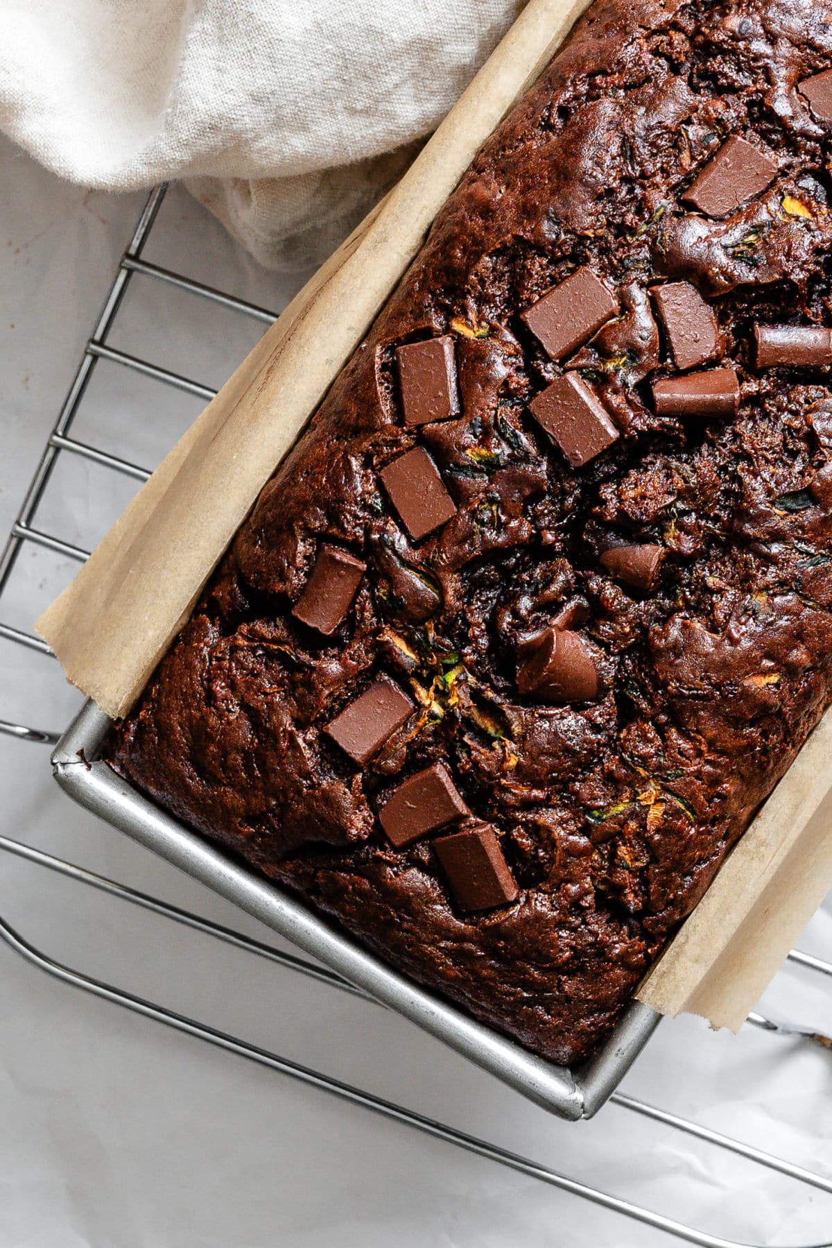 Baked chocolate zucchini bread in a pan on a wire cooling rack.