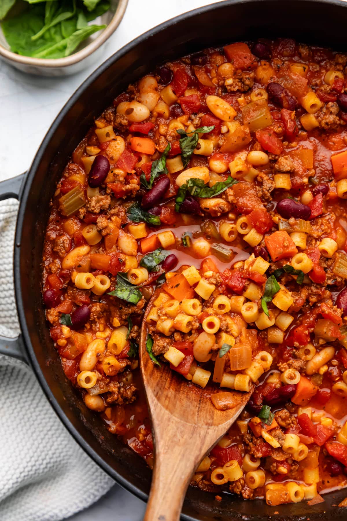 Pasta e Fagioli Soup Recipe A Dutch oven of pasta e fagioli soup next to a cream knit napkin.