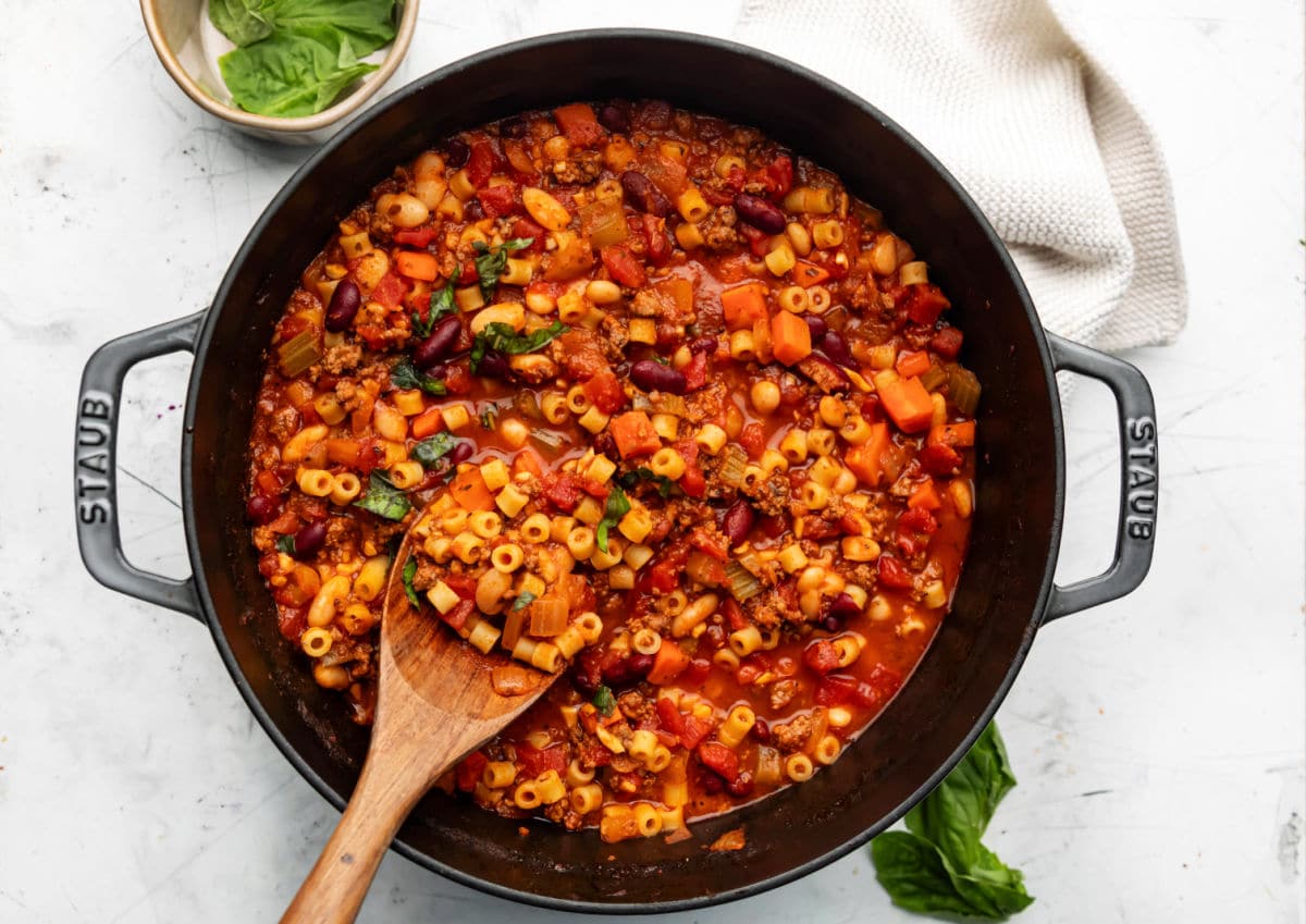 Olive Garden Copycat Pasta e Fagioli Soup Recipe A Dutch oven with pasta e fagioli soup in it next to a dish of fresh basil.