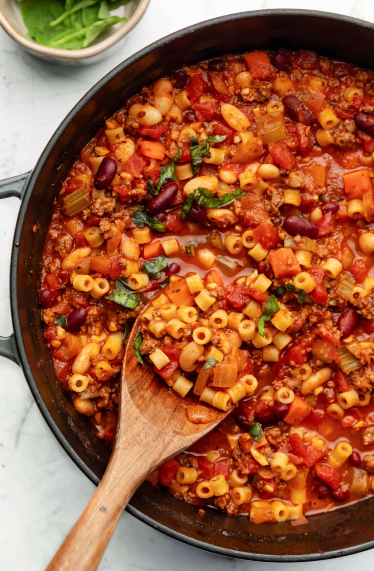 Pasta e Fagioli Soup Recipe A wooden spoon scooping up pasta e fagioli soup from a Dutch oven.