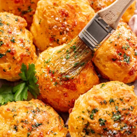 A pastry brush brushing garlic butter on cheddar bay biscuits.