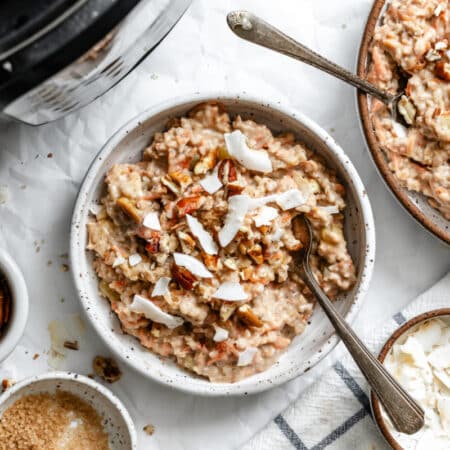 Two bowls of overnight carrot cake oatmeal next to dishes of pecans and coconut.