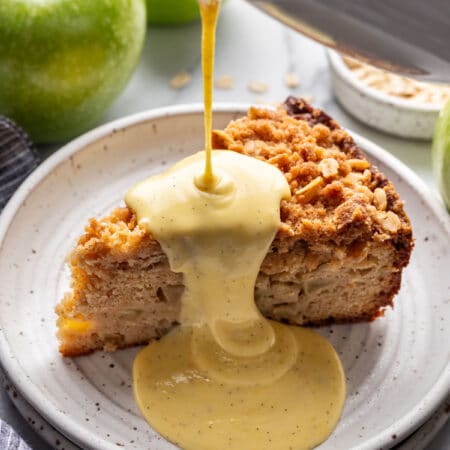 Custard sauce pouring onto a slice of Irish apple cake.