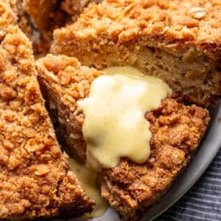 A slice of Irish apple cake with custard on top of it on a platter.