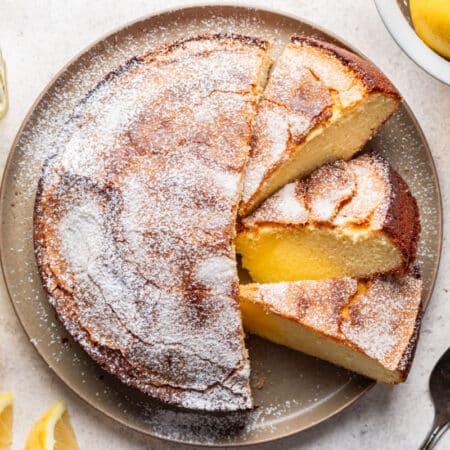 Lemon olive oil cake on a plate with three cut slices next to it.