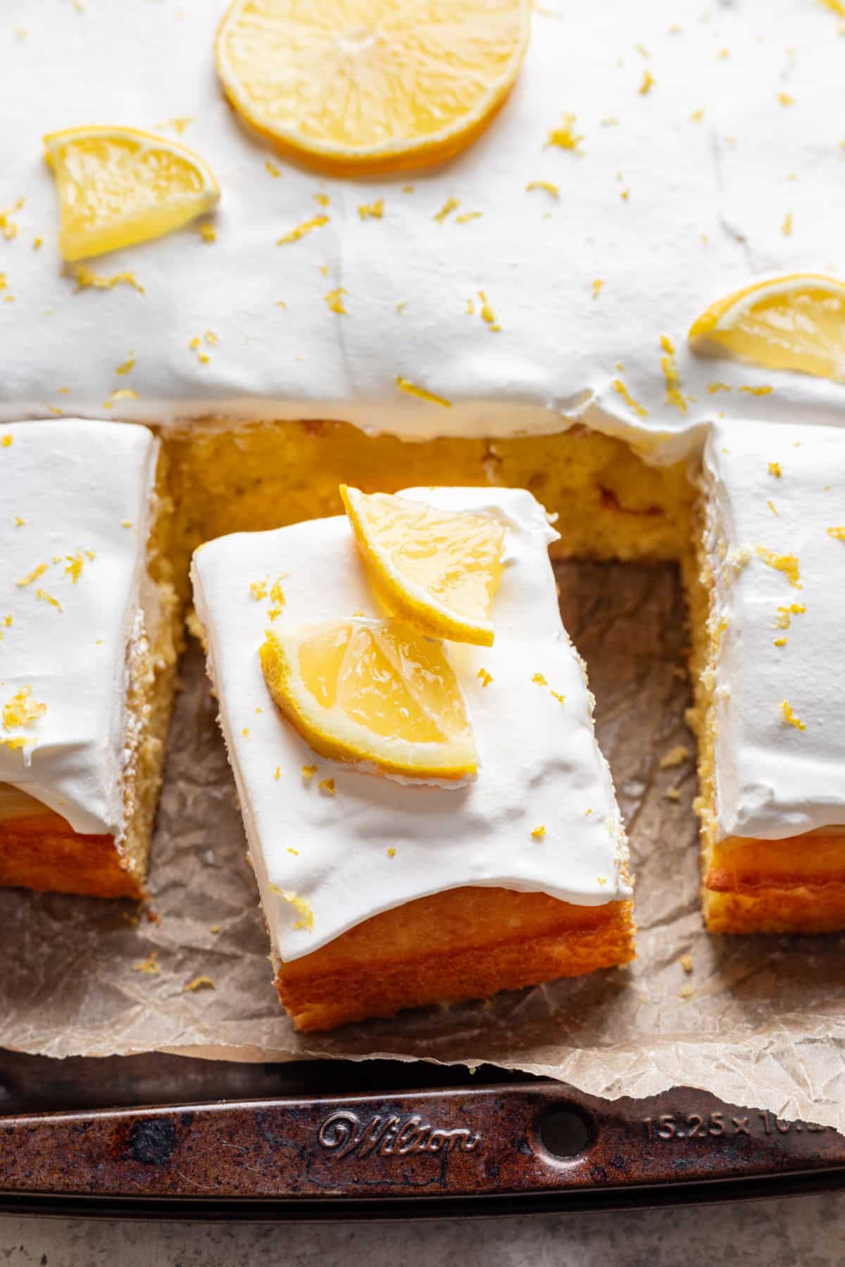 Un morceau de gâteau poke citron à côté du gâteau entier.