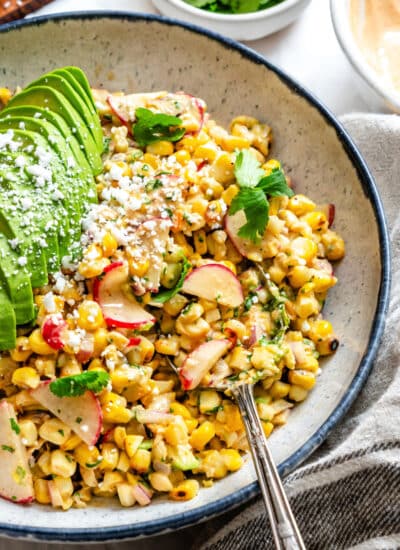 A silver spoon in a dish of Mexican street corn salad.