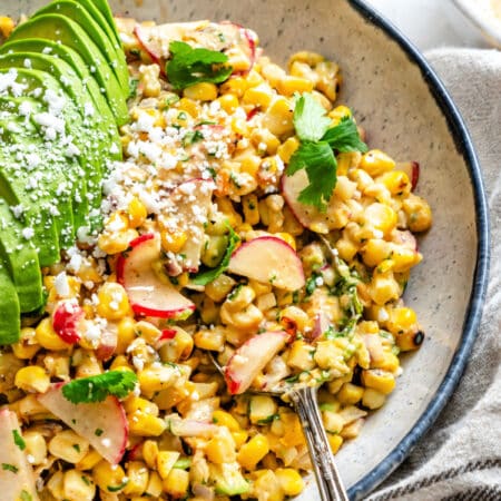 A silver spoon in a dish of Mexican street corn salad.