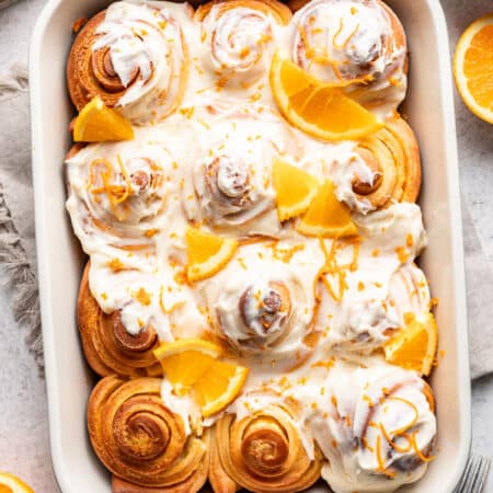Orange rolls in a baking dish topped with fresh orange wedge pieces and orange zest.