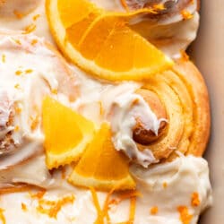Close up photo of an orange roll topped with two partial orange slices and orange zest.
