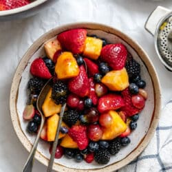 A dish of orange fruit salad next to the bowl of fruit salad.