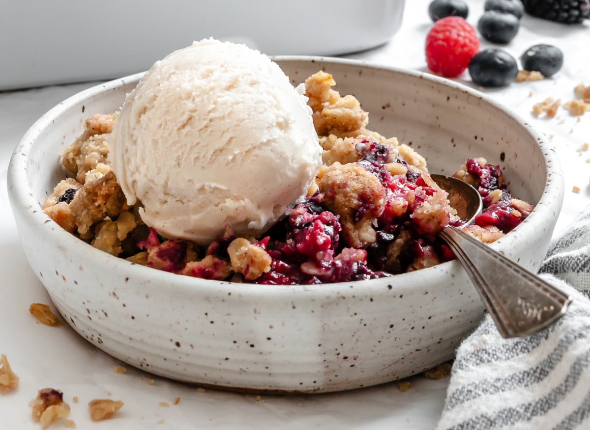 A bowl of triple berry crisp topped with a scoop of vanilla ice cream.