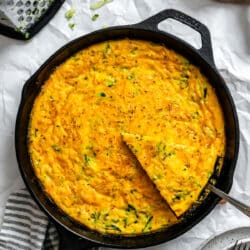 A server removing a piece of zucchini frittata from a cast iron skillet.