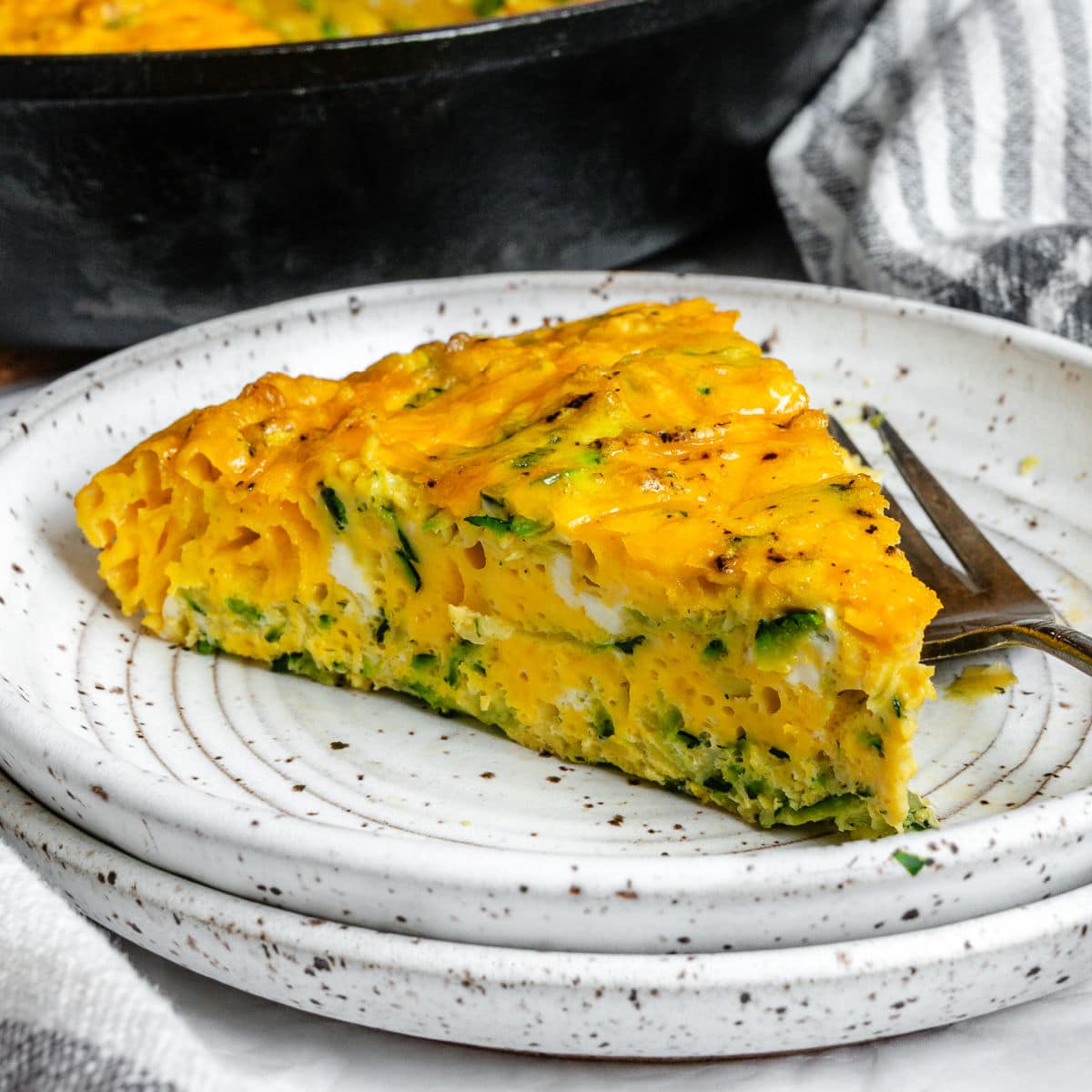 A slice of zucchini frittata on two speckled plates.