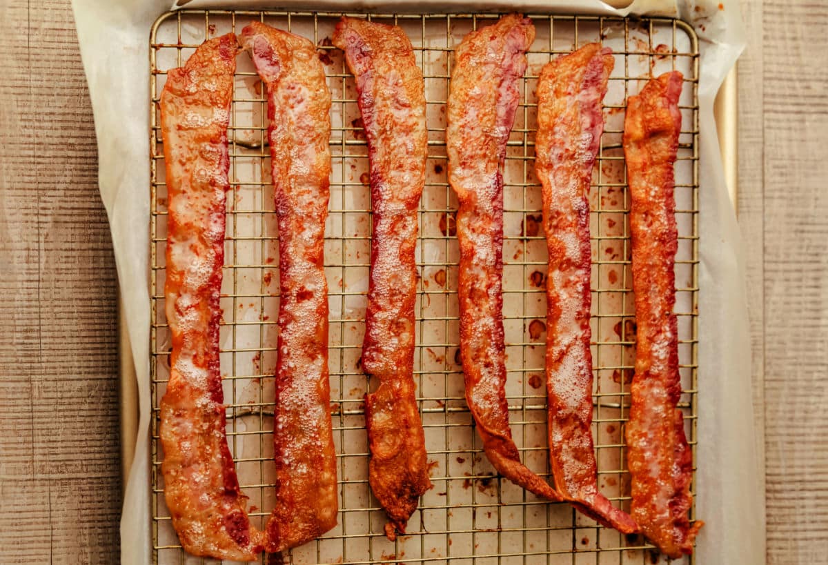 A sheet pan with cooked bacon on a parchment paper lined baking rack.