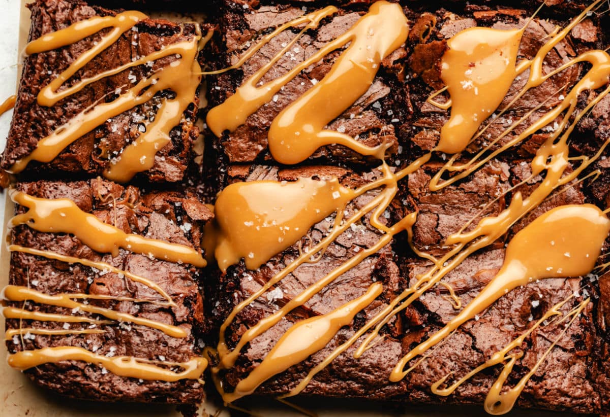 Caramel brownies drizzled with caramel on a piece of brown parchment paper.
