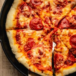 A server lifting a slice of pizza from the skillet.