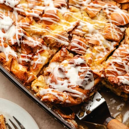 A wood handled server picking up a piece of cinnamon roll bread pudding.