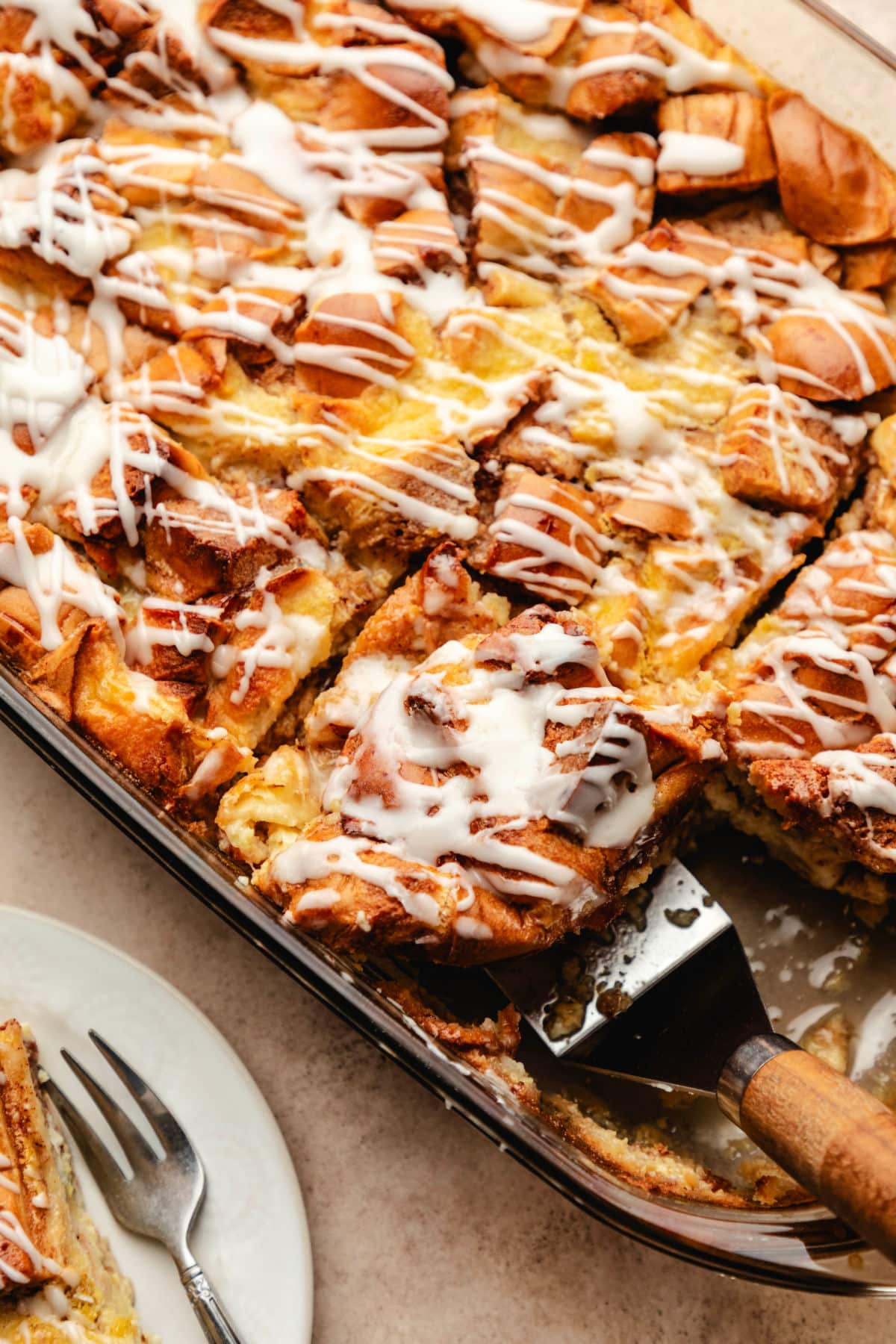 A wood handled server picking up a piece of cinnamon roll bread pudding.