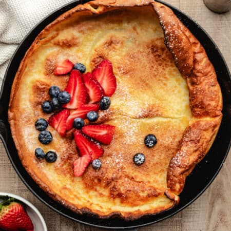 German pancake in a gray cast iron skillet topped with sliced strawberries and blueberries.