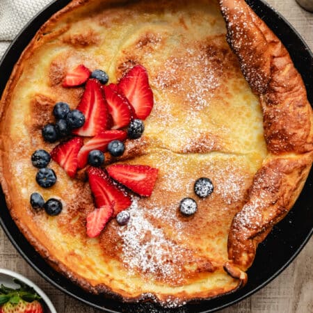 A German pancake next to a dish of fresh strawberries.