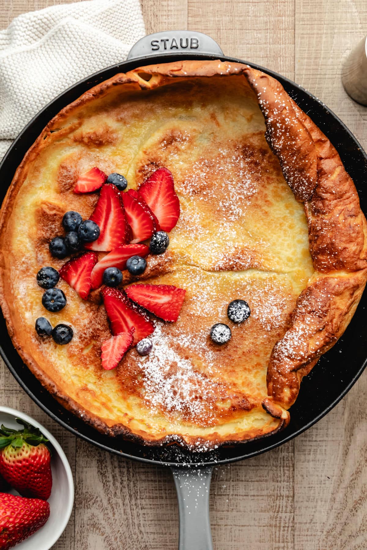 A German pancake next to a dish of fresh strawberries.