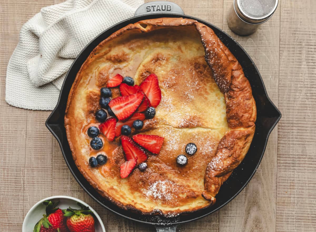 A German pancake topped with powdered sugar fresh berries and syrup.