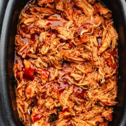 Two forks in a slow cooker filled with brown sugar bourbon bbq chicken.