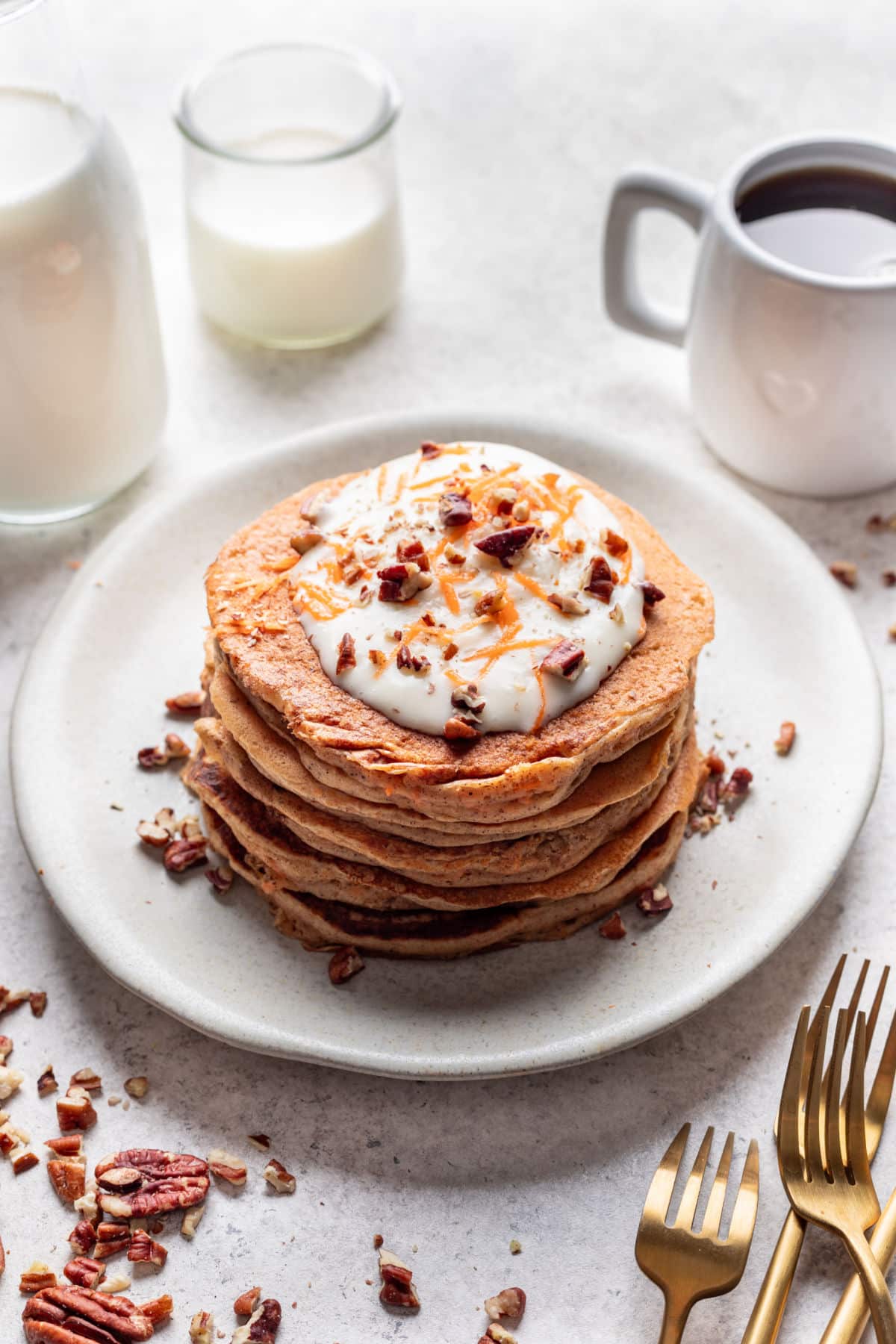 A stack of carrot cake pancakes topped with cream cheese frosting and toasted pecans.