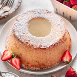 A chiffon cake dusted with powdered sugar next to some fresh strawberries.