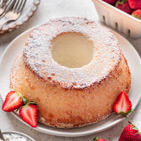 A chiffon cake dusted with powdered sugar next to some fresh strawberries.