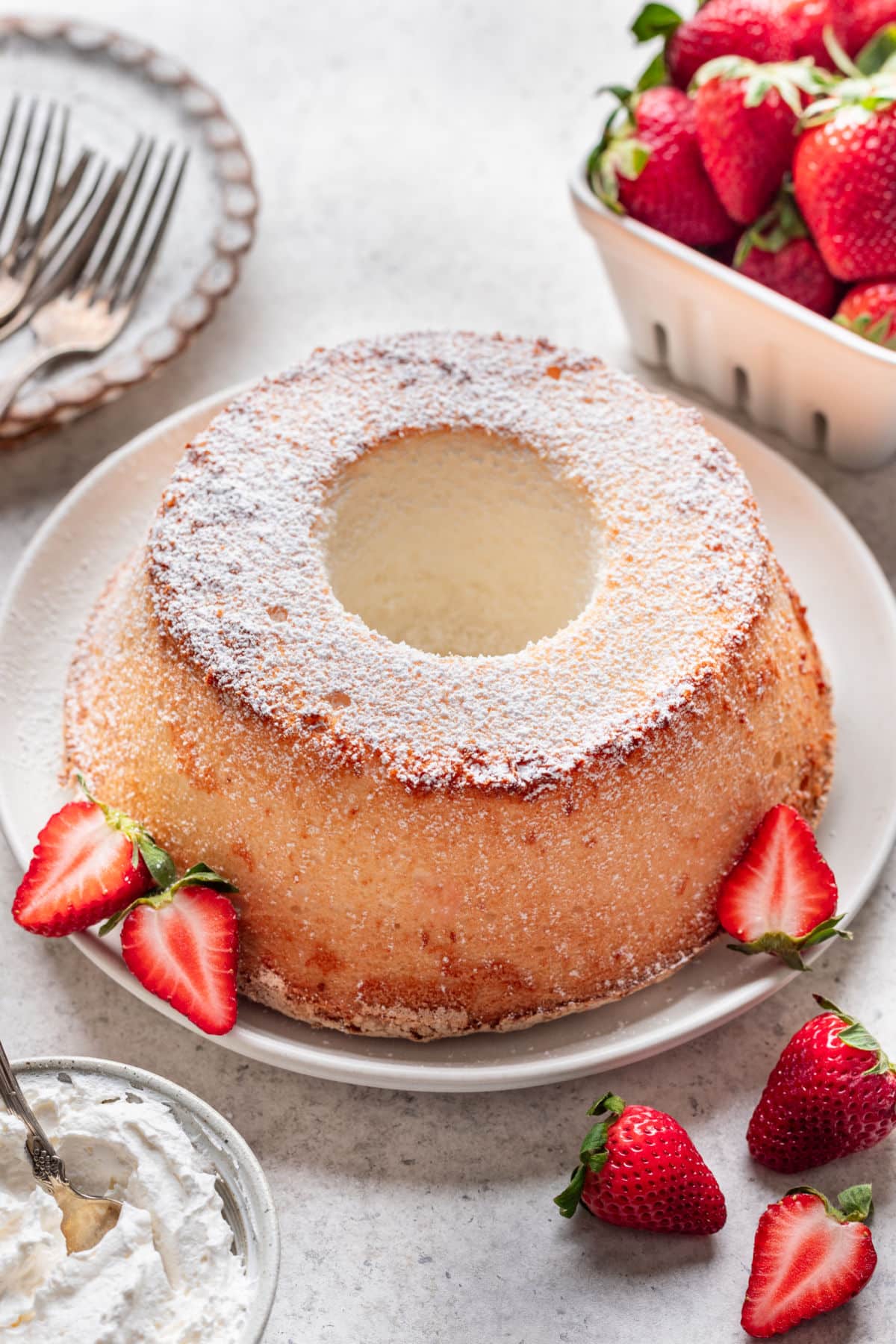 A chiffon cake dusted with powdered sugar next to some fresh strawberries.