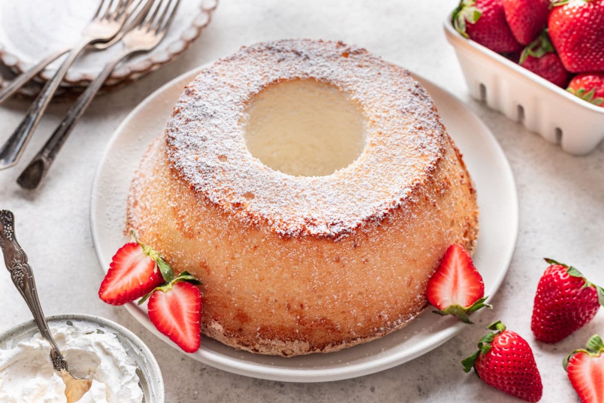 A chiffon cake on a platter with a few fresh strawberries on it.