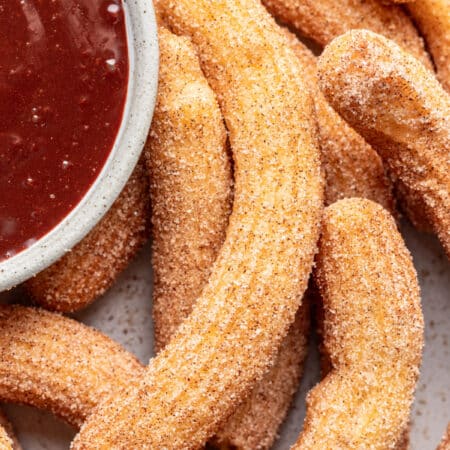 Homemade churros next to a dish of chocolate dipping sauce on a platter.