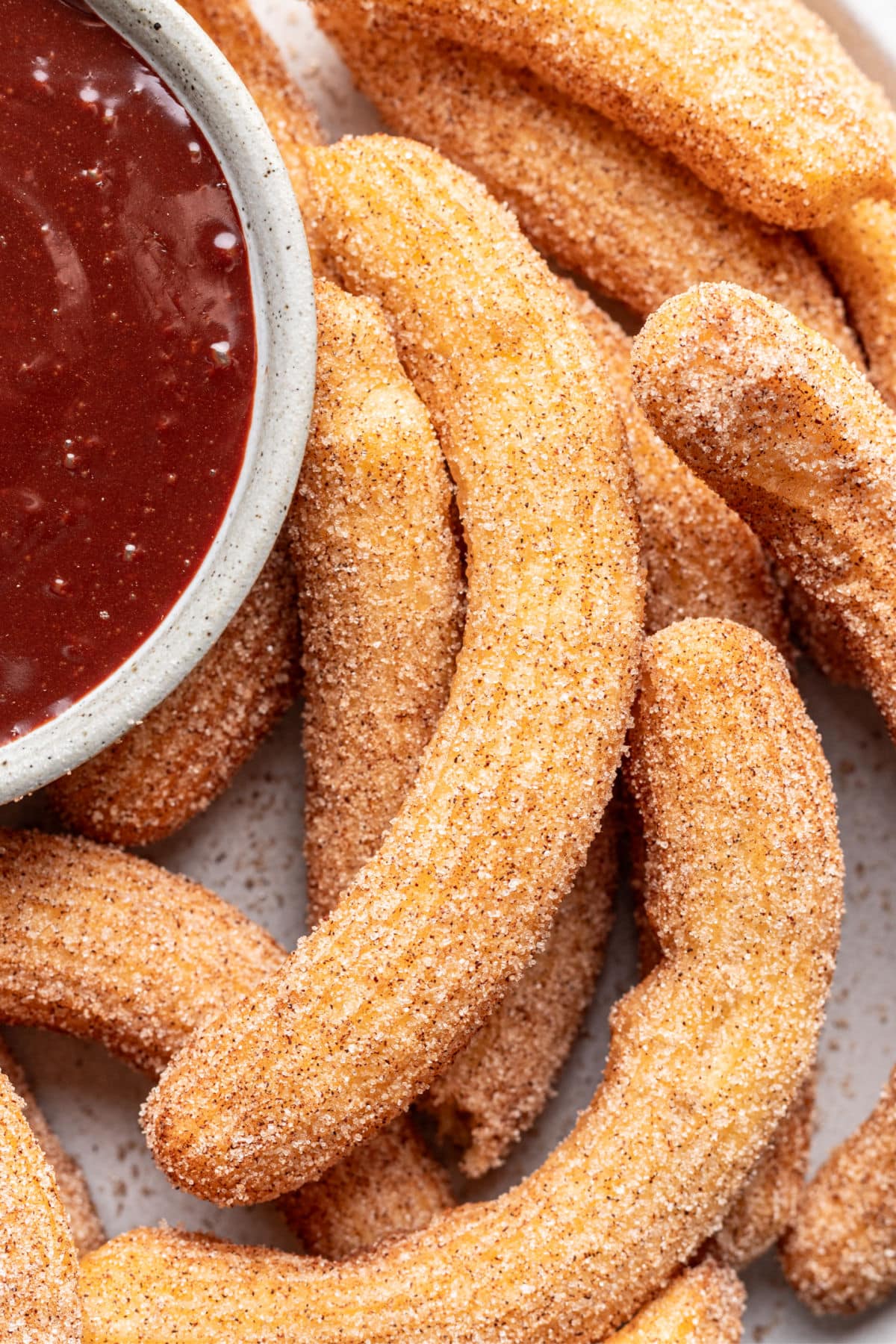 Homemade churros next to a dish of chocolate dipping sauce on a platter.